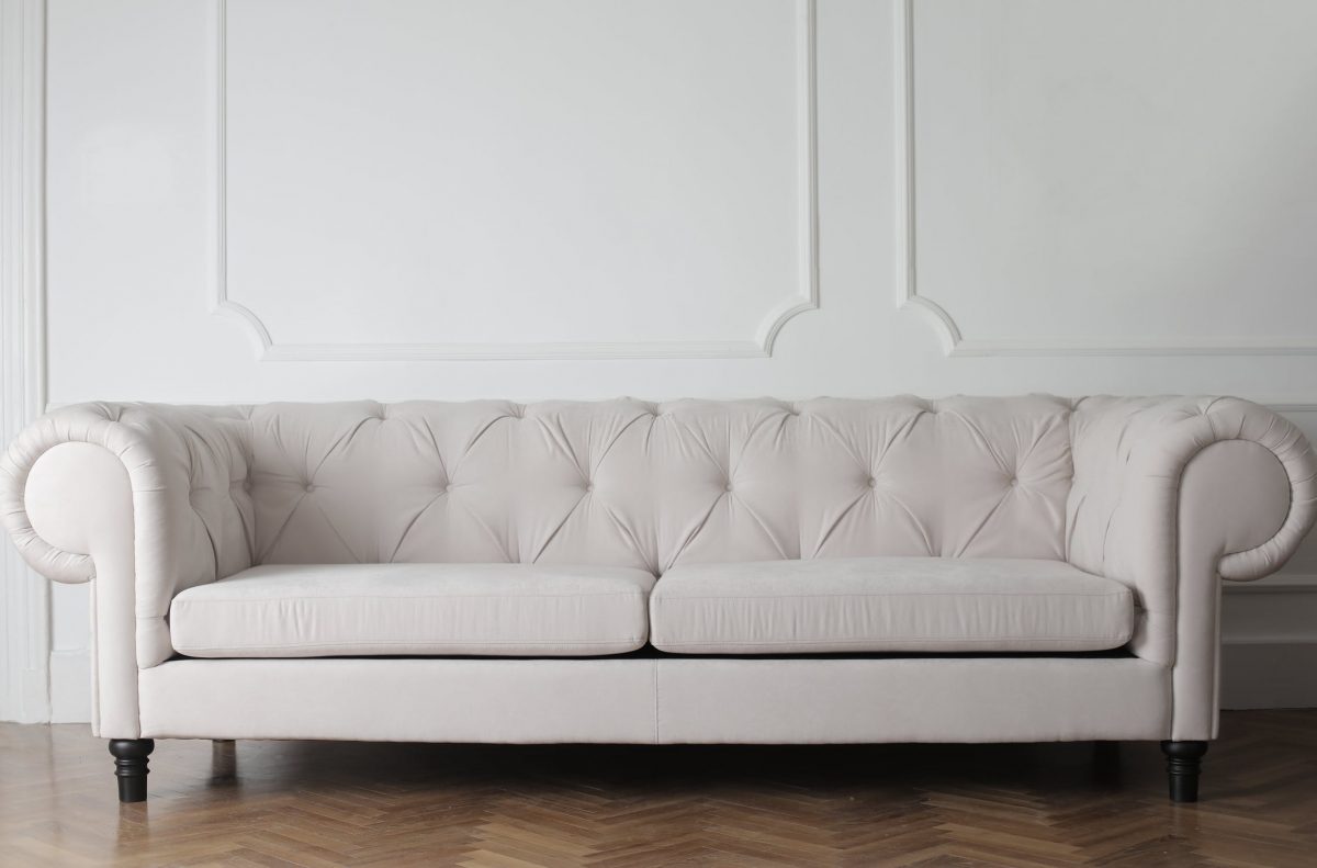 a light colored couch against a white wall and on dark hardwood floors